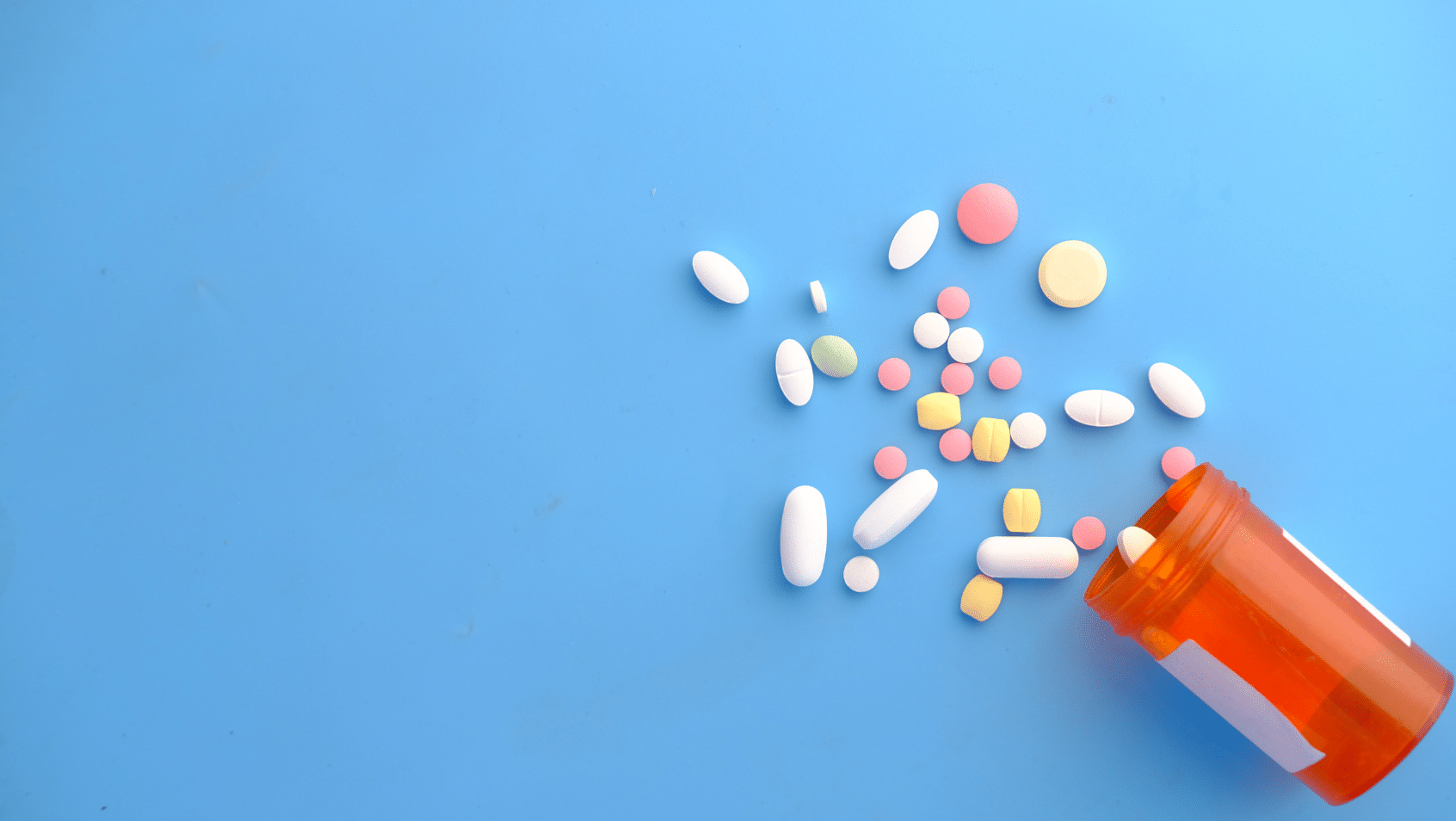 Pills spill out from an orange prescription bottle on a blue background